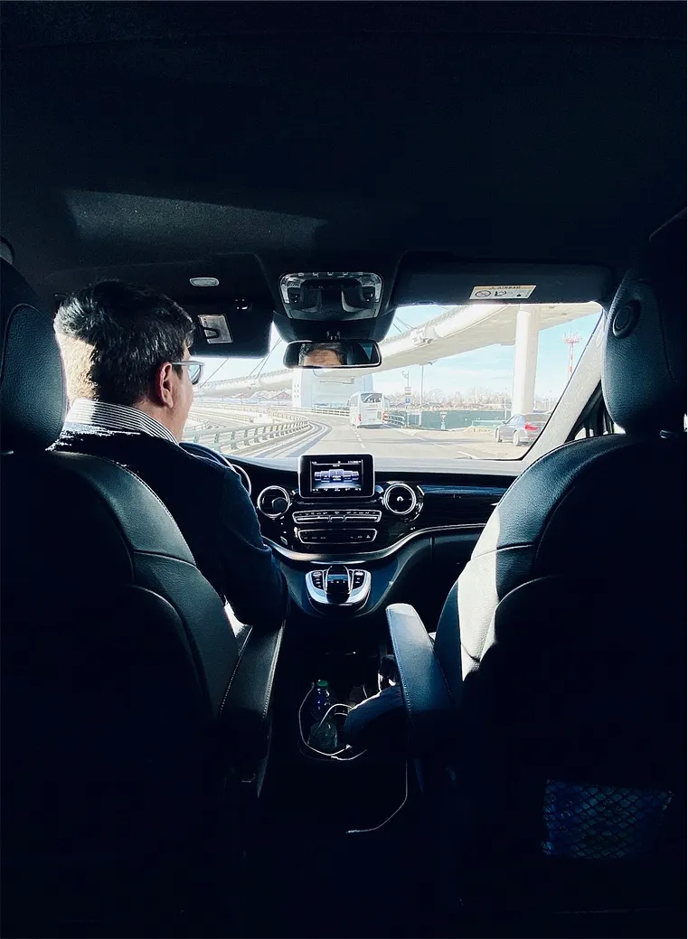 Chauffeur en veste au volant d'un Mercedes Classe V, vu depuis la banquette arrière